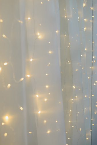 blurred led light wall garland on white tulle fabric backdrop, festive decoration, vertical stock photo image background