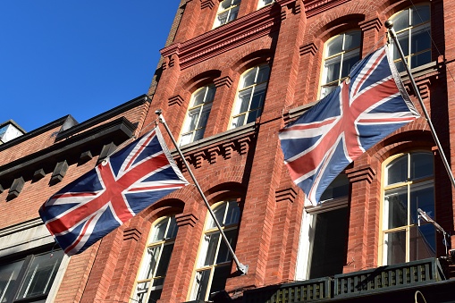 Picture of british flags, union jack flying in the wind on a traditional facade made of red bricks.
