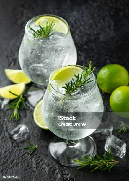 Gin And Tonic Alcohol Drink With Lime Rosemary And Ice On Rustic Black Table Stock Photo - Download Image Now