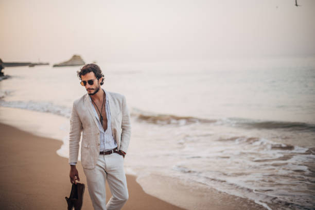 Modern guy taking a walk on the beach Handsome, modern man in casual, white suit, holding his shoes and taking a walk on the beach. hot handsome man stock pictures, royalty-free photos & images