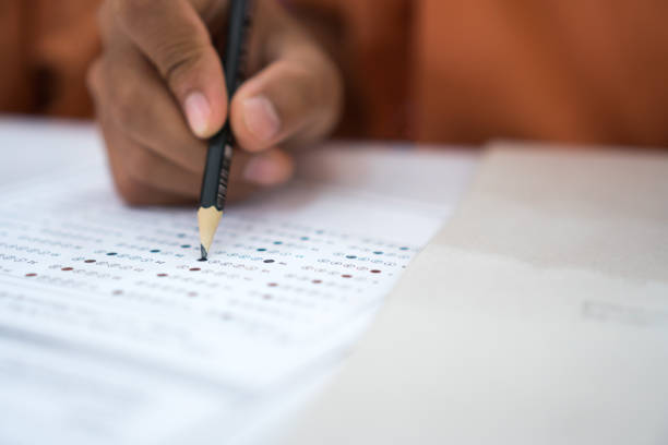 istock Exam test school or university concept : Hand student holding pencil writing standardized answer multiple carbon paper form with gray black answers sheet bubbled of question in examination assessment. 1177834579