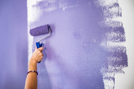 Young Woman Painting Wall Purple.