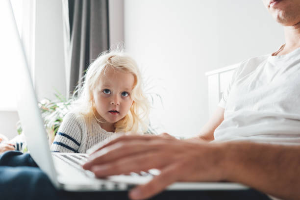 istock Father working on laptop while his daughter looking on screen. Young dad sits on bed with children using the computer together at home 1177837697