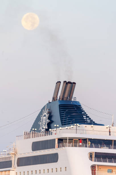 Smoke stacks of cruise ship under full moon in Venice in St.Mark basic (bacino di San Marco) at sunrise while moonset.\nSeen from Riva San Biasio.