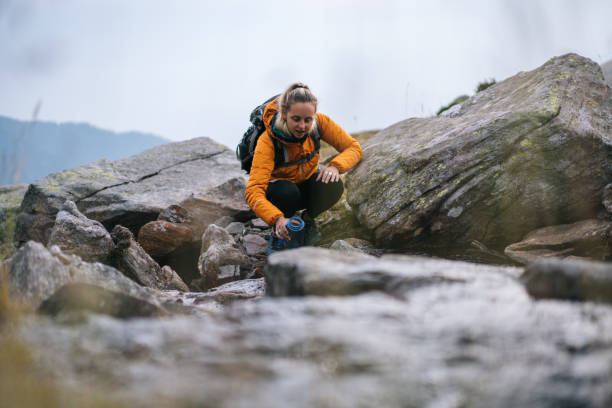 a mulher nova caminhadas acima de uma inclinação rochosa nas montanhas - water bottle sports and fitness selective focus sport - fotografias e filmes do acervo