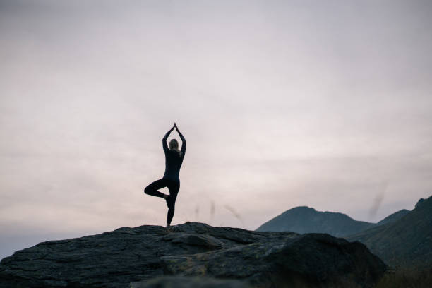 Woman performs yoga moves on rock in mountains