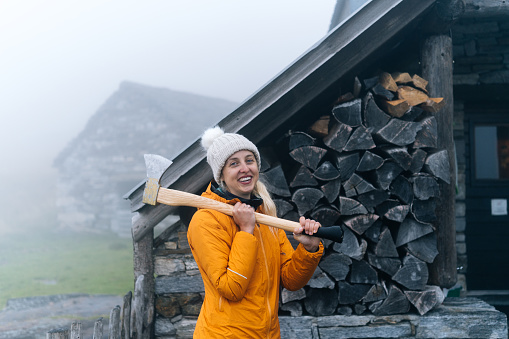 She is standing beside the wood pile holding the axe