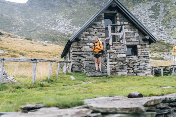 Hiker stands on stone cabin steps in mountain meadow