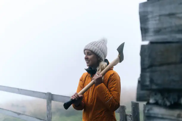 Photo of Young woman prepares to chop wood at hut in mountains