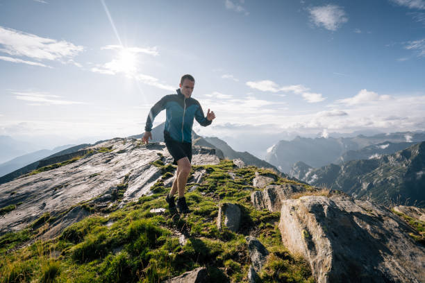 le coureur de sentier se limite le long d'une crête de montagne dans la lumière - cross coat photos et images de collection