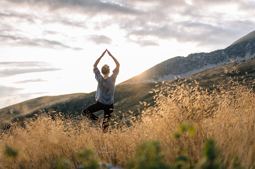Young woman preforms yoga in mountains in morning light