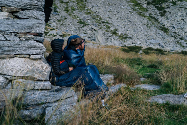 istock Couple in sleeping bags lean against rock wall 1177858017