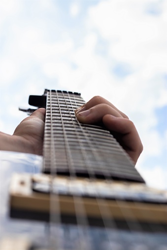 Male hand playing electric guitar and bending the strings with blue cloudy sky in the background