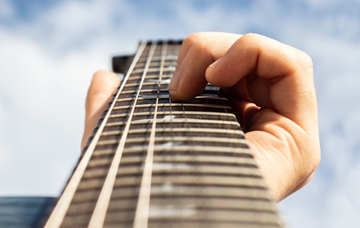 Male hand fingers in electric guitar fretboard with cloudy sky in the background. Focus on fingers