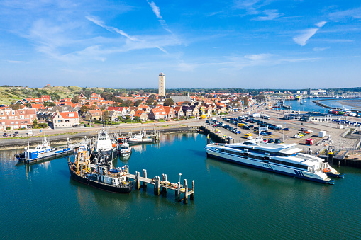 Netherlands, Terschelling - Aug 25, 2019: Brandaris lighthouse towers up. Catamaran MS Tiger moored to a wharf and other vessels along piers, in the harbour of West-Terschelling, West Frisian Islands.