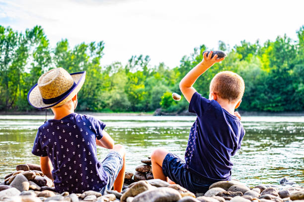 Rear view boys throwing rocks at riverbank