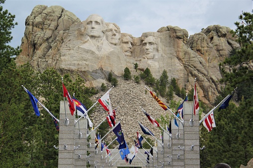 The four presidents on Mount Rushmore are shown in soft light with the Avenue of Flags in the foreground.