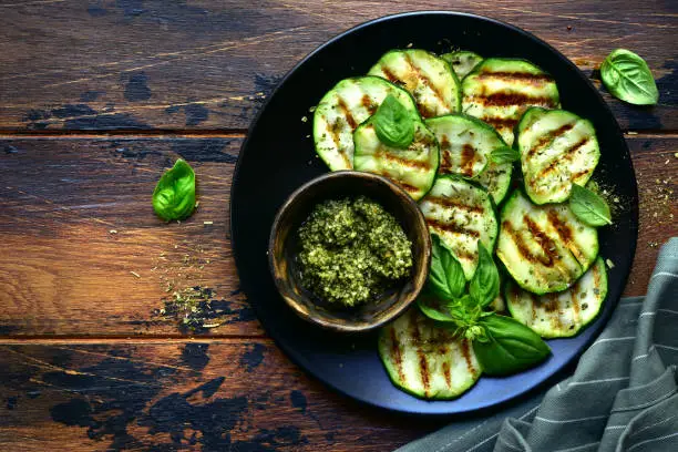 Grilled zucchini slices with basil pesto on a black plate over dark wooden background.Top view with copy space.
