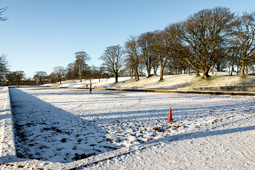 An alley and a large empty pond covered by snow at the entrance to Duthie park, Aberdeen, Scotland. Photo taken in the morning after unusual snowfall in December 2017.