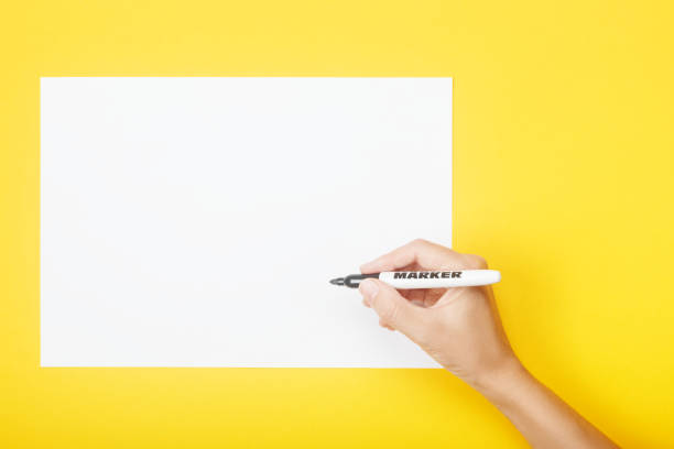 istock Hand with marker over blank paper on a yellow background. Mock up with copy space for your ideas. 1177881162