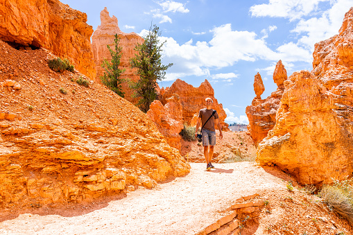 Man tourist person walking by orange color formations at Queens Garden Navajo Loop trail at Bryce Canyon National Park in Utah