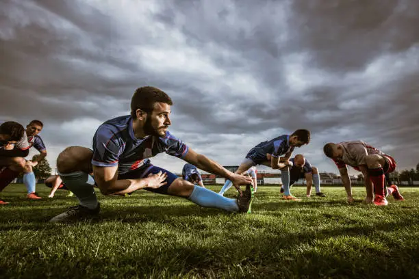 Large group of athletes stretching before a match on playing field. Focus is on man in the foreground. Copy space.