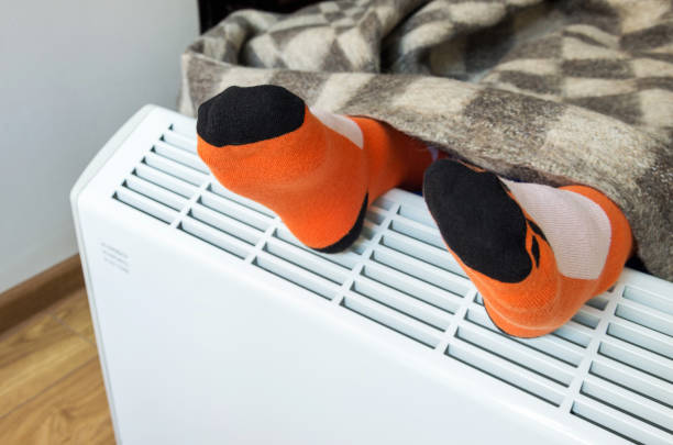 A child with a woolen blanket warms his feet over an electric heater. Symbolic image of cold and flu, home heating in the cold season. Close-up, selective focus. A child with a woolen blanket warms his feet over an electric heater. Symbolic image of cold and flu, home heating in the cold season. Close-up, selective focus. warms stock pictures, royalty-free photos & images