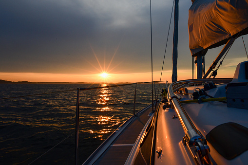 Boat deck of a sailboat empty with no people in the evening, Winde, buoy and lots of red colored ropes hanging around, beautiful sunset sky above the sea in the background