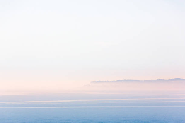 Minimalist landscape scene of Sandwich Bay, Kent on a misty but bright summer morning. The town of Deal peninsular can just be seen through the mist and there is a soft glow of sunrise. Minimalist landscape scene of Sandwich Bay, Kent on a misty but bright summer morning. The town of Deal peninsular can just be seen through the mist and there is a soft glow of sunrise. sandwich kent stock pictures, royalty-free photos & images