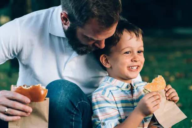 Photo of Father consoling crying son with delicious burger