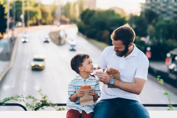 Photo of Father and son eating delicious burgers in the city