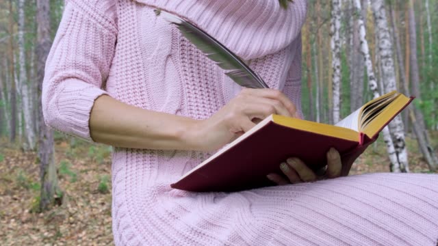 Happy attractive smiling woman writes poetry with feather in spring forest.