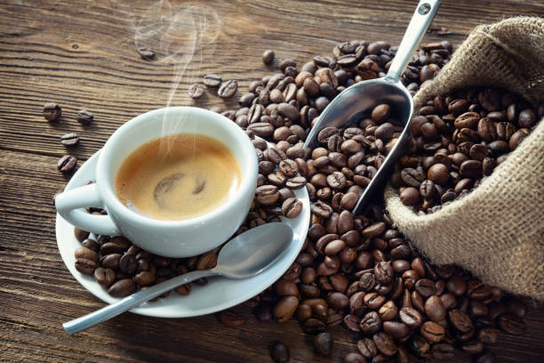 Cup of espresso with coffee beans Cup of espresso with coffee beans, bag, scoop and steam on rustic wooden background roasted coffee bean stock pictures, royalty-free photos & images