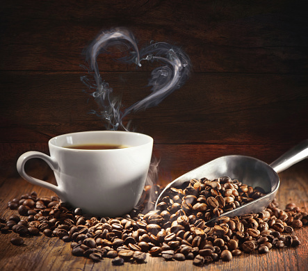 Coffee cup and coffee beans with bag, scoop and steam in heart shape on dark wooden background