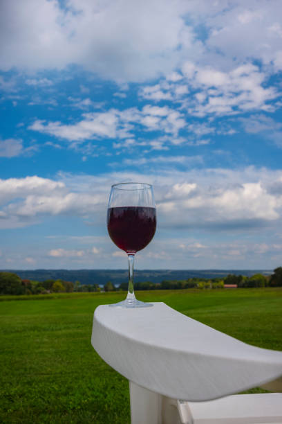 A glass of red wine photographed at on the arm rest of a white, plastic Adirondack chair near Cayuga Lake in the Finger Lakes Region of New York State. A glass of red wine photographed at on the arm rest of a white, plastic Adirondack chair near Cayuga Lake in the Finger Lakes Region of New York State. finger lakes stock pictures, royalty-free photos & images