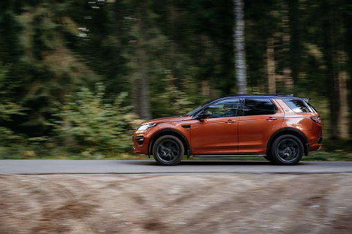 Minsk, Belarus - September 24, 2019: borwn color car Land Rover Discovery Sport fast moving on country road in green autumn forest.