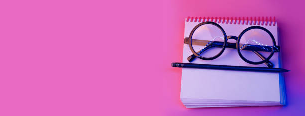 istock black round glasses lie on a Notepad in neon light on pink background 1177911821