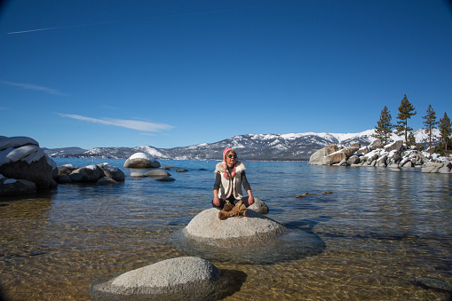 Female meditating on a rock in the water at Lake Tahoe