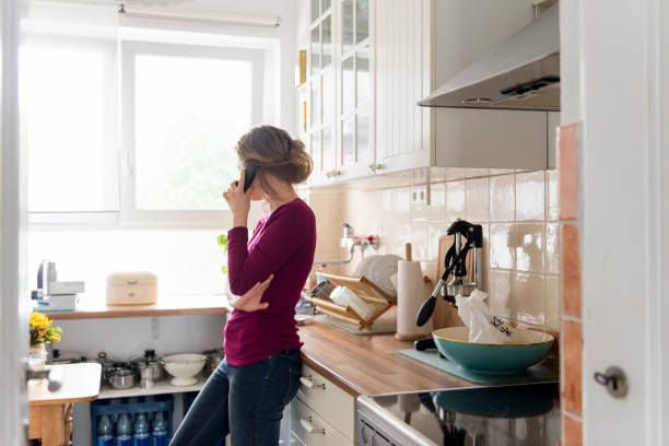 una joven de pie en casa en su cocina mientras hace una llamada telefónica - cordless phone telephone landline phone telephone receiver fotografías e imágenes de stock