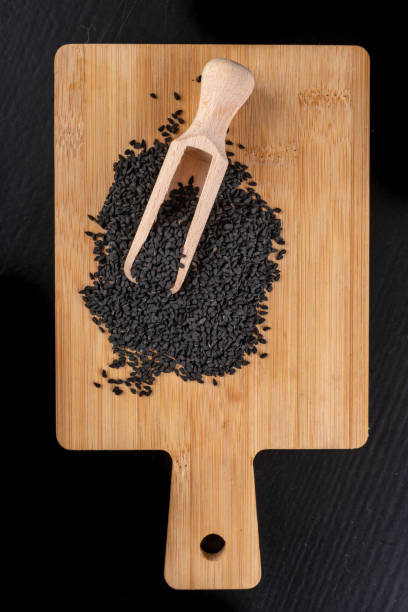 gesunde und schmackhafte schwarze kreuzkümmelbohnen auf einem holzbrett. zutaten für eine gesunde ernährung in einer modernen küche. dunkle hintergrund. - nigella sativa stock-fotos und bilder