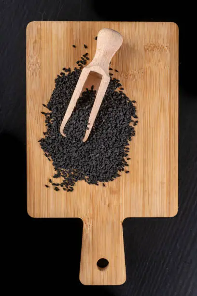 Healthy and tasty black cumin beans on a wooden board. Ingredients for a healthy diet in a modern kitchen. Dark background.