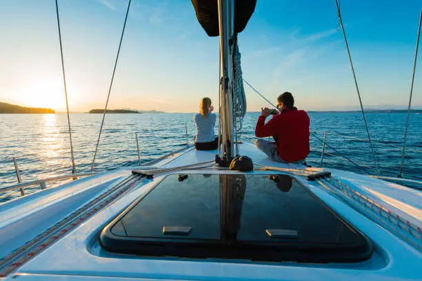 Young couple taking photos with smart phone on sailboat at sunset Taken by Sony a7R II, 42 Mpix.