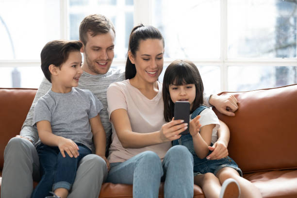 istock Happy parents with cute kids sit on sofa using phone 1177915997