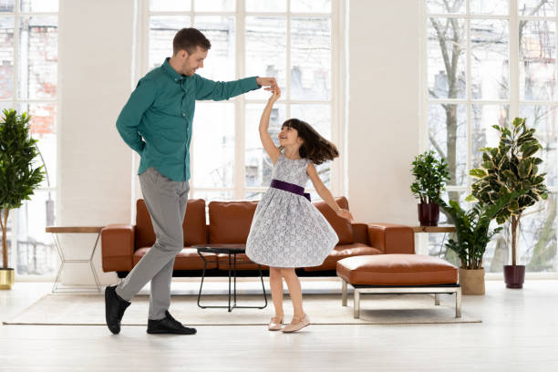 Loving dad dancing with happy cute little daughter at home Loving young dad dancing with happy cute little daughter holding hand of kid girl princess wearing dress, caring father teaching waltz small child playing in living room enjoy time together at home dancing dad stock pictures, royalty-free photos & images