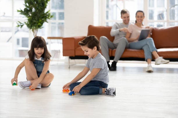 genitori che si rilassano usando il dispositivo sul divano, i bambini giocano a terra - floor two parent family couple home interior foto e immagini stock