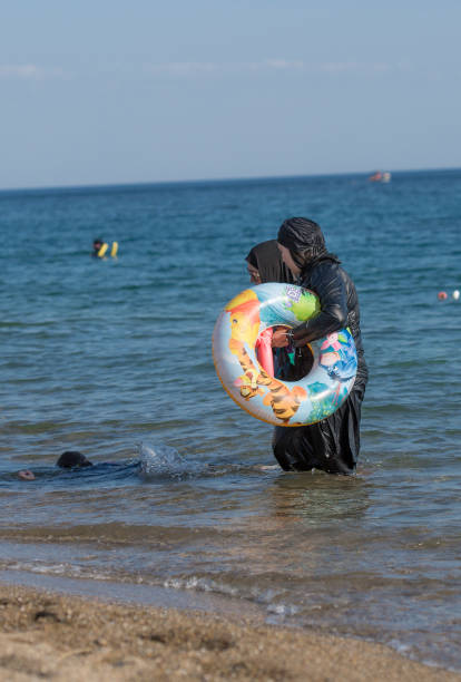 穆斯林婦女在海上與五顏六色的游泳輪。穆斯林婦女穿著黑色布基尼（伊斯蘭女性泳衣）。 - 回教泳裝 圖片 個照片及圖片檔