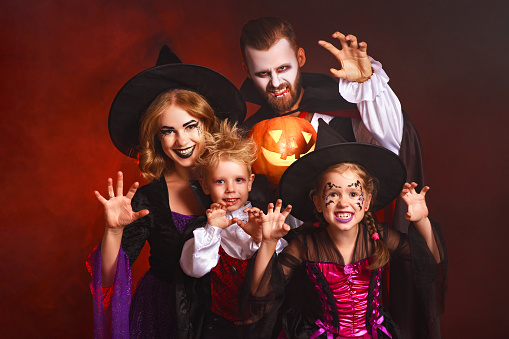 happy family mother father and children in costumes and makeup on a celebration of Halloween on dark red background