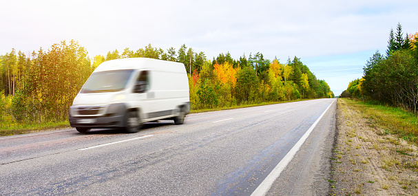 Van fast moving on asphalt road in the countryside on autumn landscape background. Small truck delivers the goods