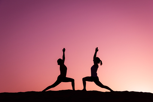 Couple of women practice warrior pose at pink twilight in Canary Islands, Spain