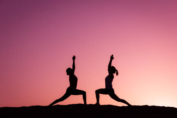 sylwetki jogina na virabhadrasana na szczycie wydm maspalomas o kolorowym zachodzie słońca - yoga flexibility two people women zdjęcia i obrazy z banku zdjęć